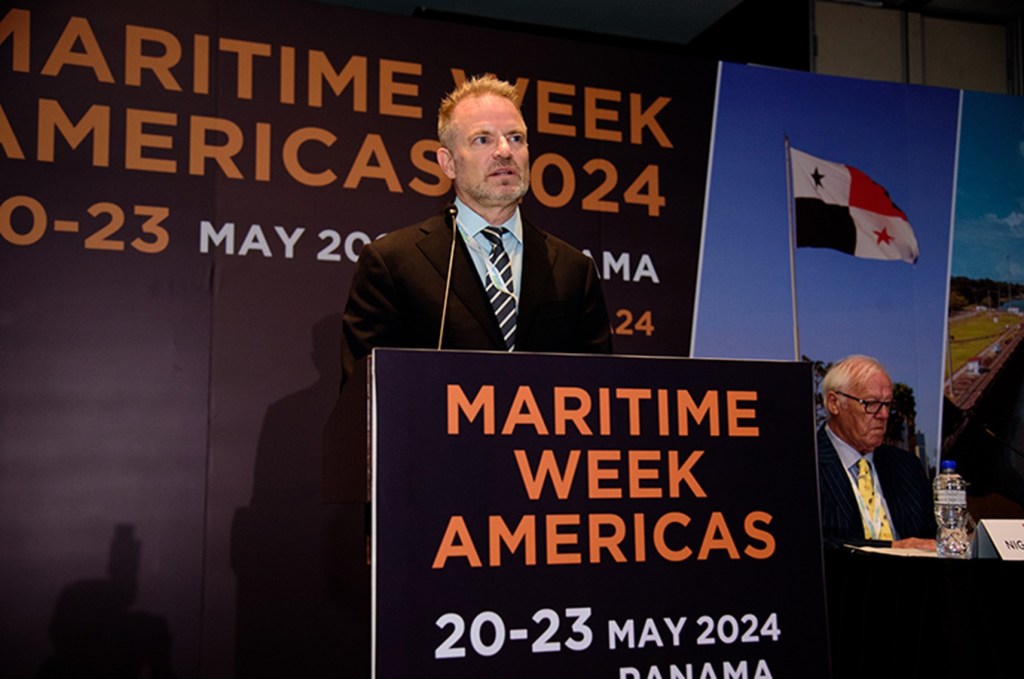 A man in a suit standing at a podium that reads Maritime Week Americas 20-23 May 2024 Panama