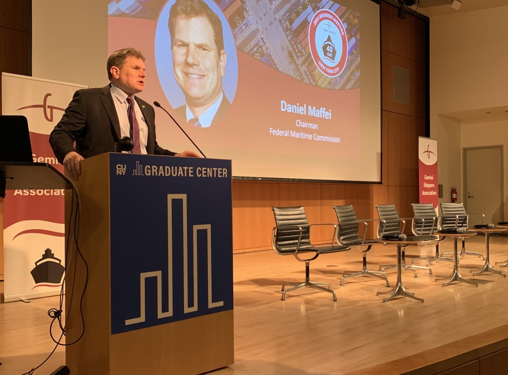 Man in a suit presenting at a podium on stage.